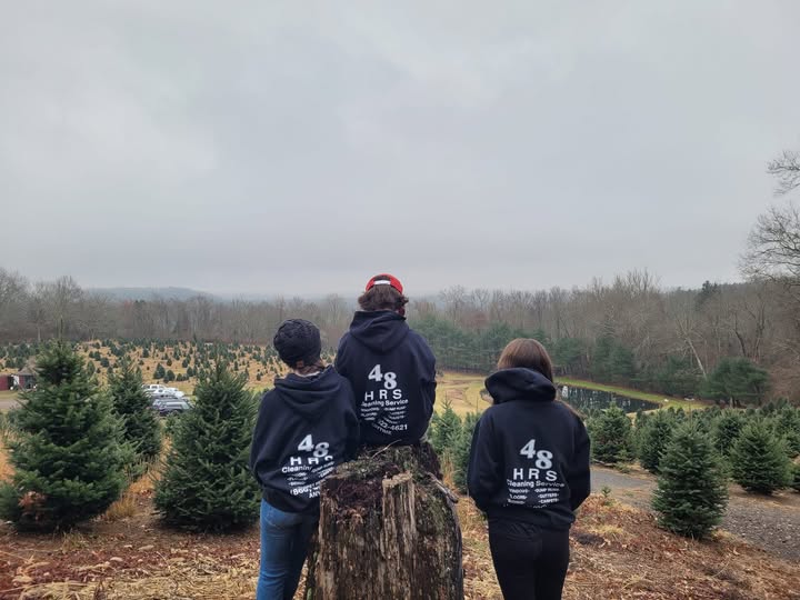 Three family members in 48 HRS hoodies looking out over a Christmas tree farm